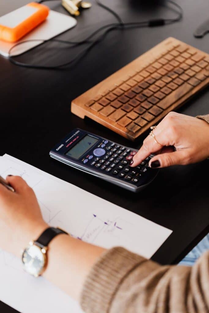 Mastering the Accounting Cycle for Small Business Success 4 From above crop anonymous female accountant working with calculator and writing down notes on paper while sitting at table with computer keyboard