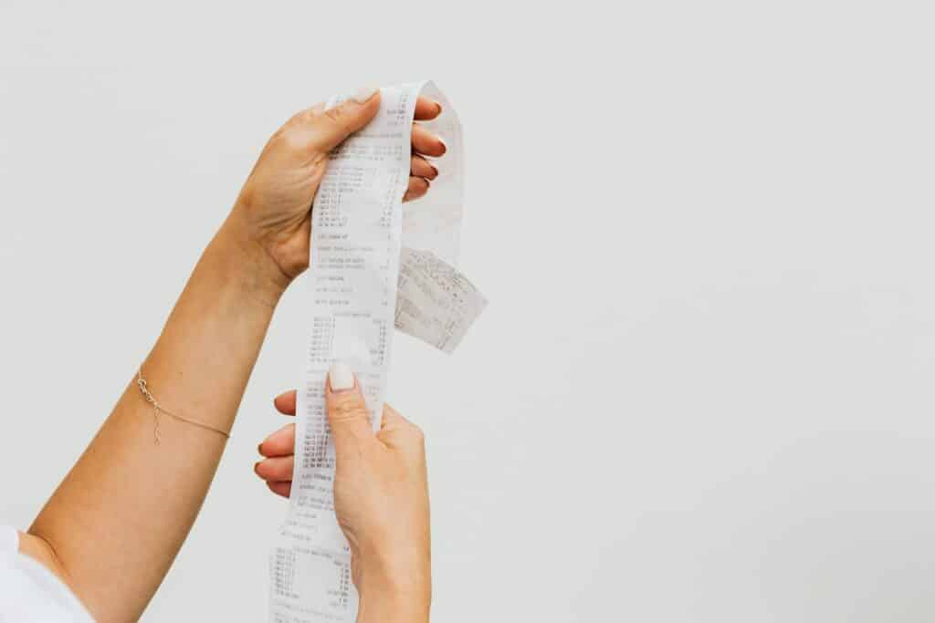A detailed view of a person holding a long shopping receipt against a plain background.