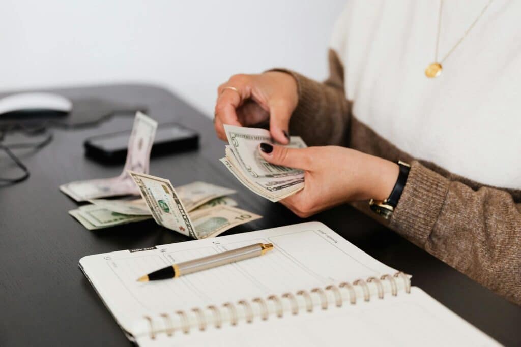 Top Bookkeeping Services for Small Businesses 3 Close-up of person counting cash with notepad on desk, indicating financial tasks.